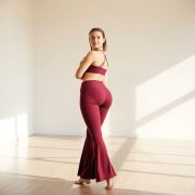 A model in burgundy flare leggings plus size flared activewear pants posing in a bright yoga studio.